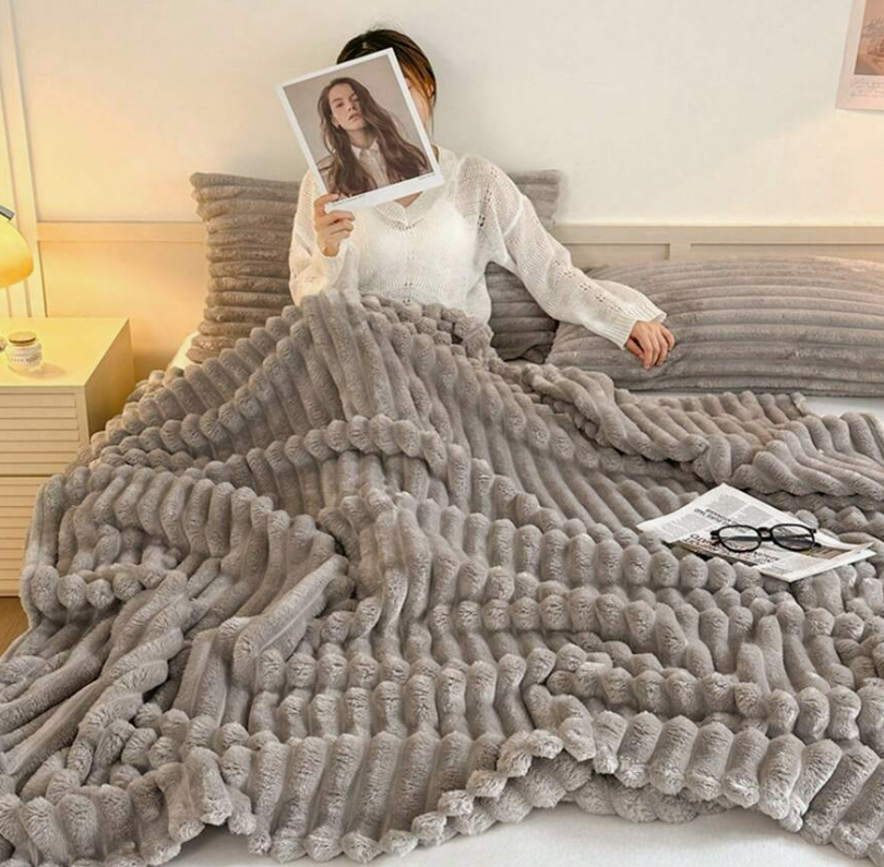 Woman relaxing on a sofa under a soft gray ribbed plush blanket