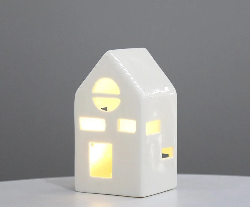 White ceramic cottage tea light house with arched window, lit warmly