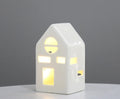 White ceramic cottage tea light house with arched window, lit warmly
